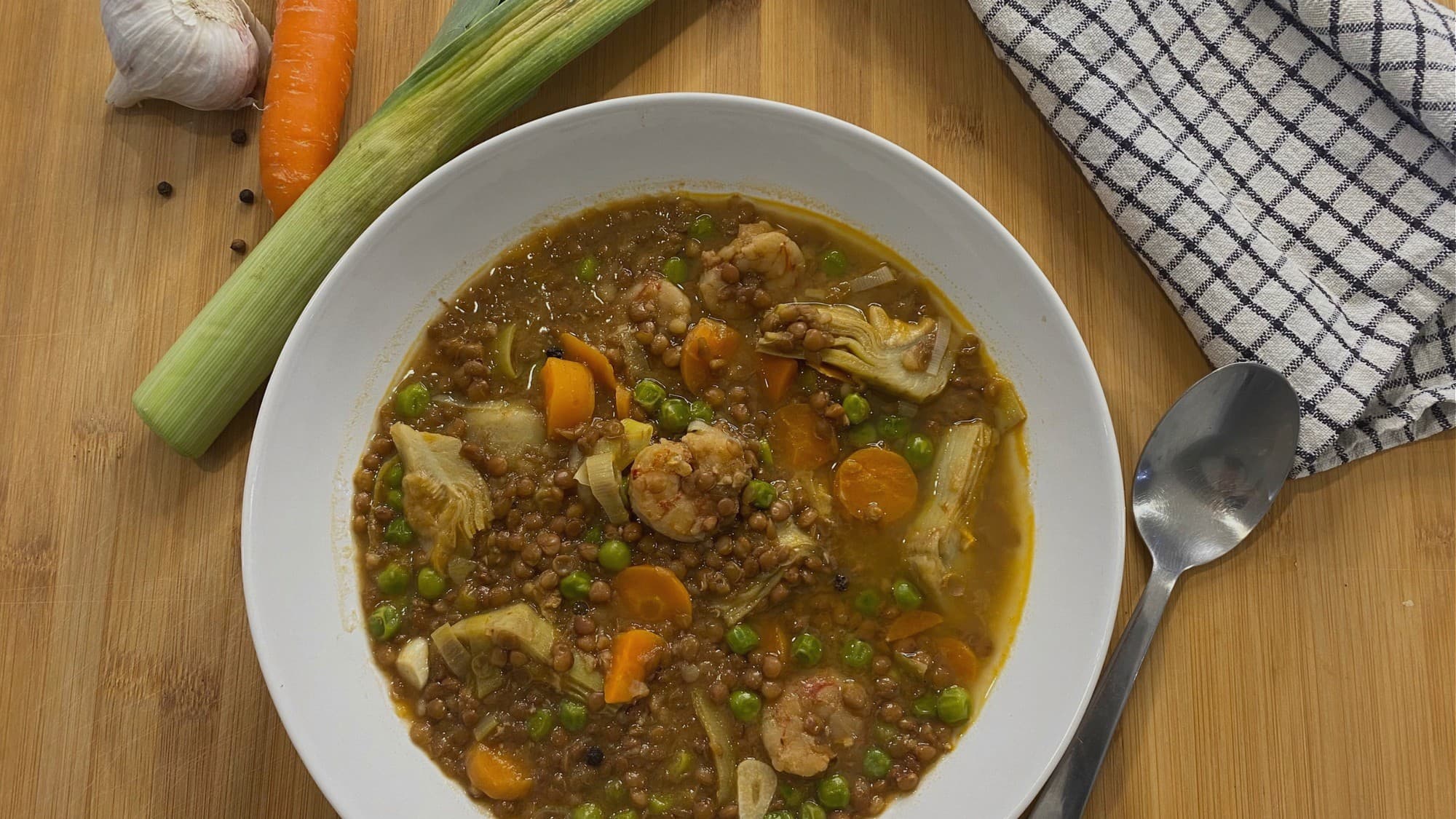 Guiso de lentejas con alcachofas, langostinos, guisantes y zanahoria, listo para servir