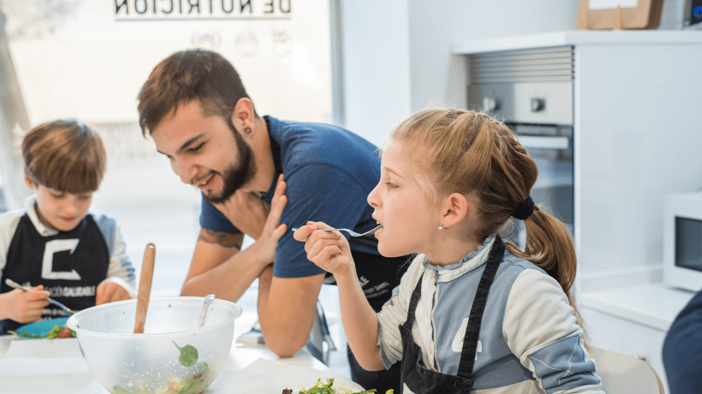 Monitor de La Habitación Saludable dando de probar una ensalada a una niña en un taller de cocina