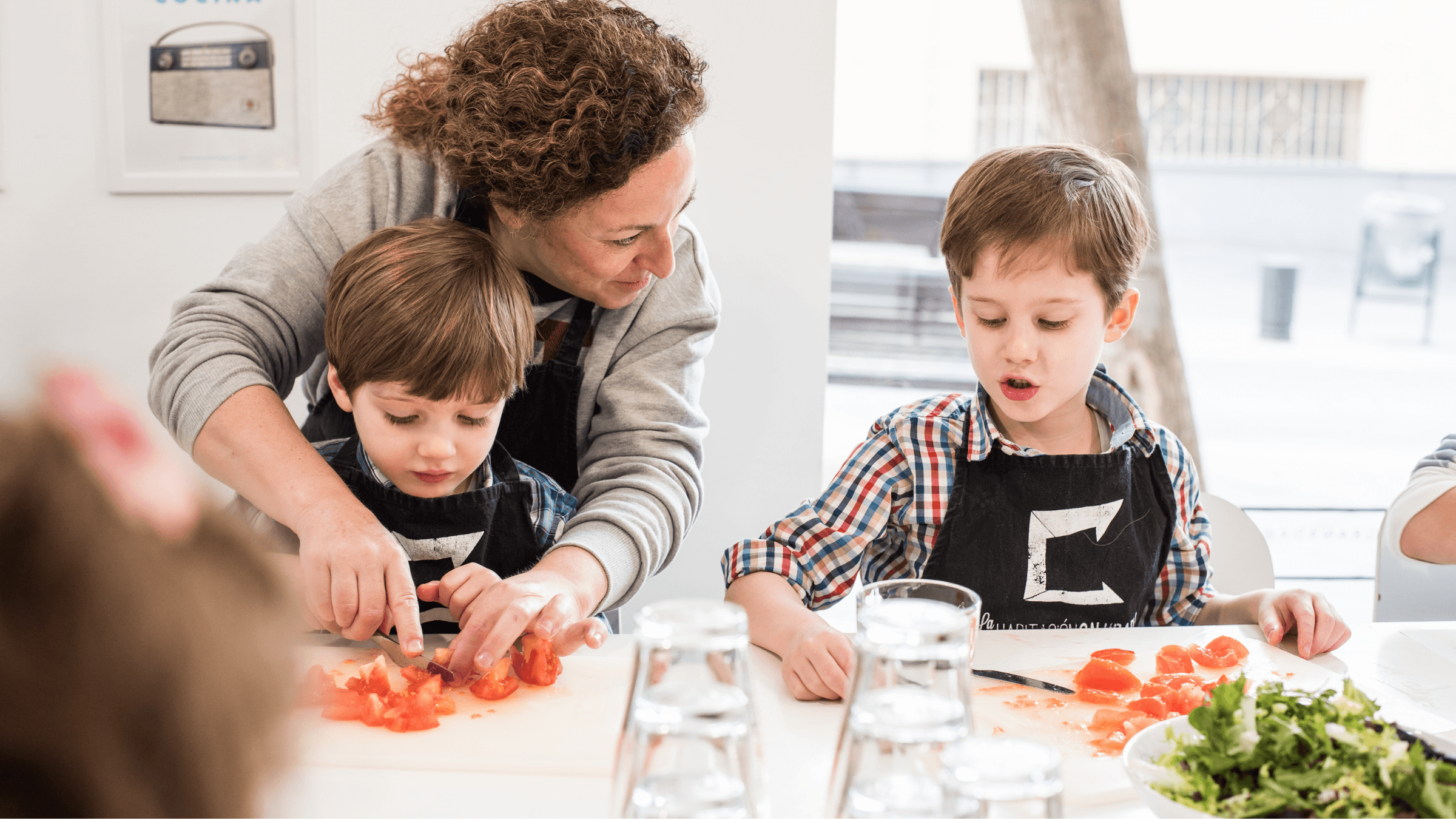 Una madre enseña a su hijo pequeño a cortar tomate en la cocina de casa