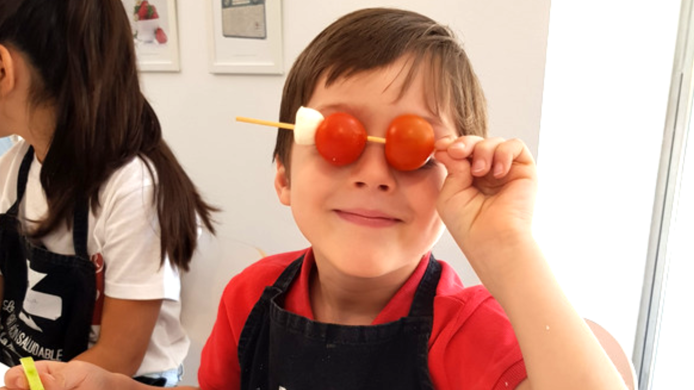Niño sonriendo con dos tomates cherry a modo de gafas en un taller de cocina de La Habitación Saludable