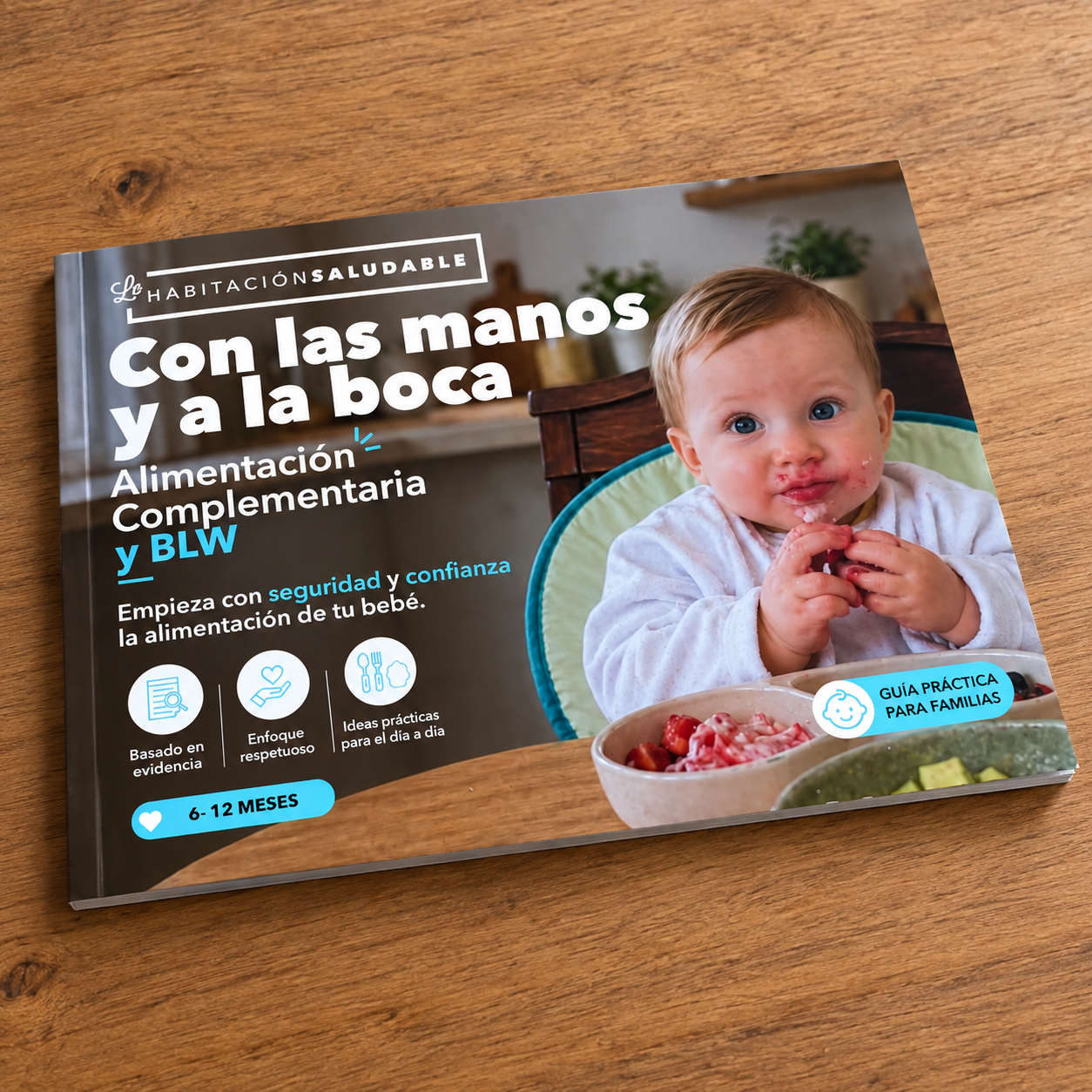 Libro 'Con las manos y a la boca', guía de alimentación complementaria y BLW de La Habitación Saludable, sobre una mesa de madera